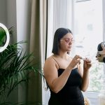 Criadora grava uma avaliação de produto em ambiente interno, diante de uma câmera e de uma luz circular.