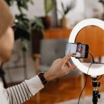 Criador de conteúdo grava um vídeo com smartphone e ring light em um ambiente interno.