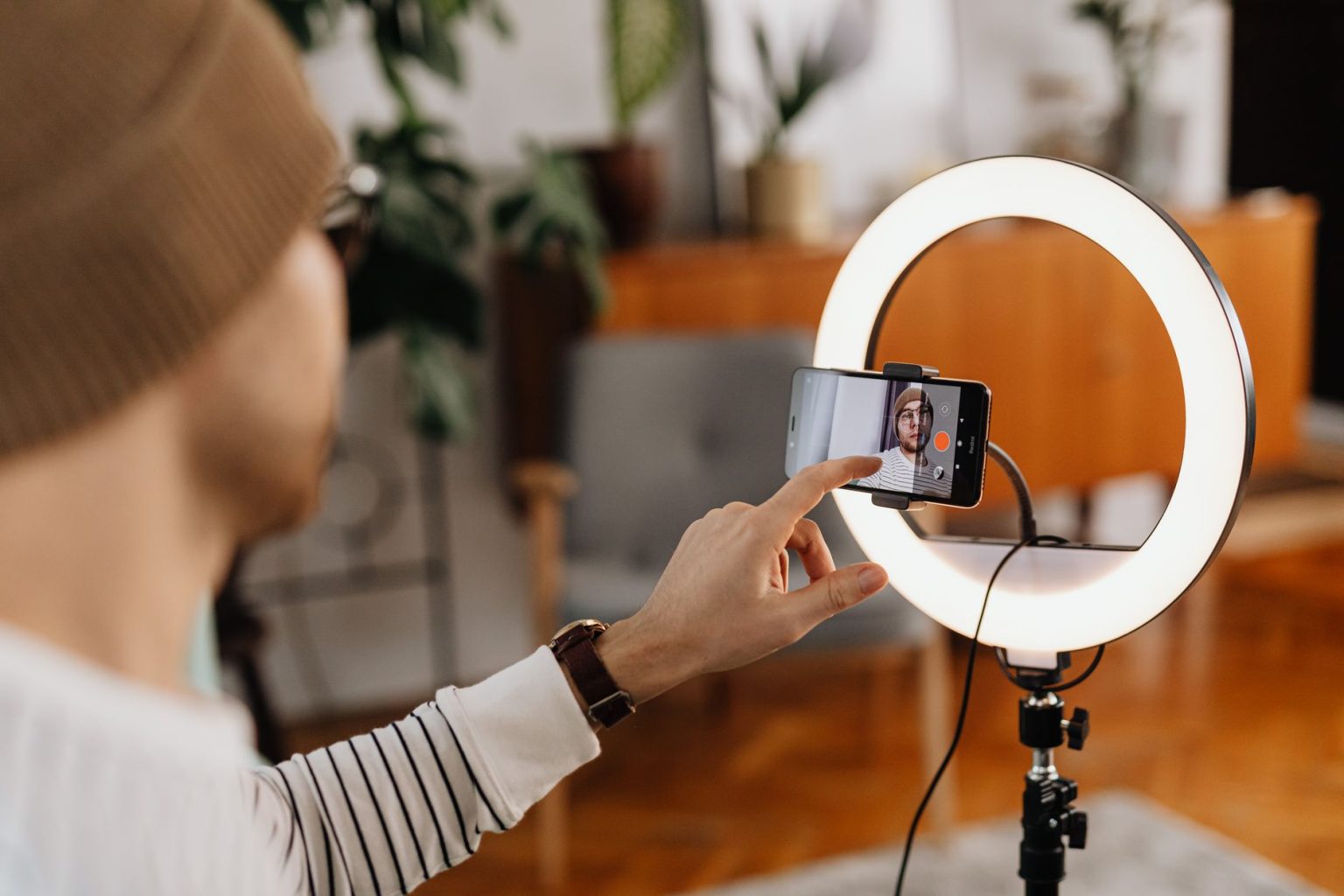 Criador de conteúdo grava um vídeo com smartphone e ring light em um ambiente interno.