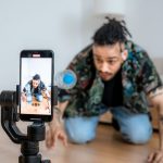 Criador de conteúdo filmando com um smartphone acoplado a um estabilizador em ambiente interno.