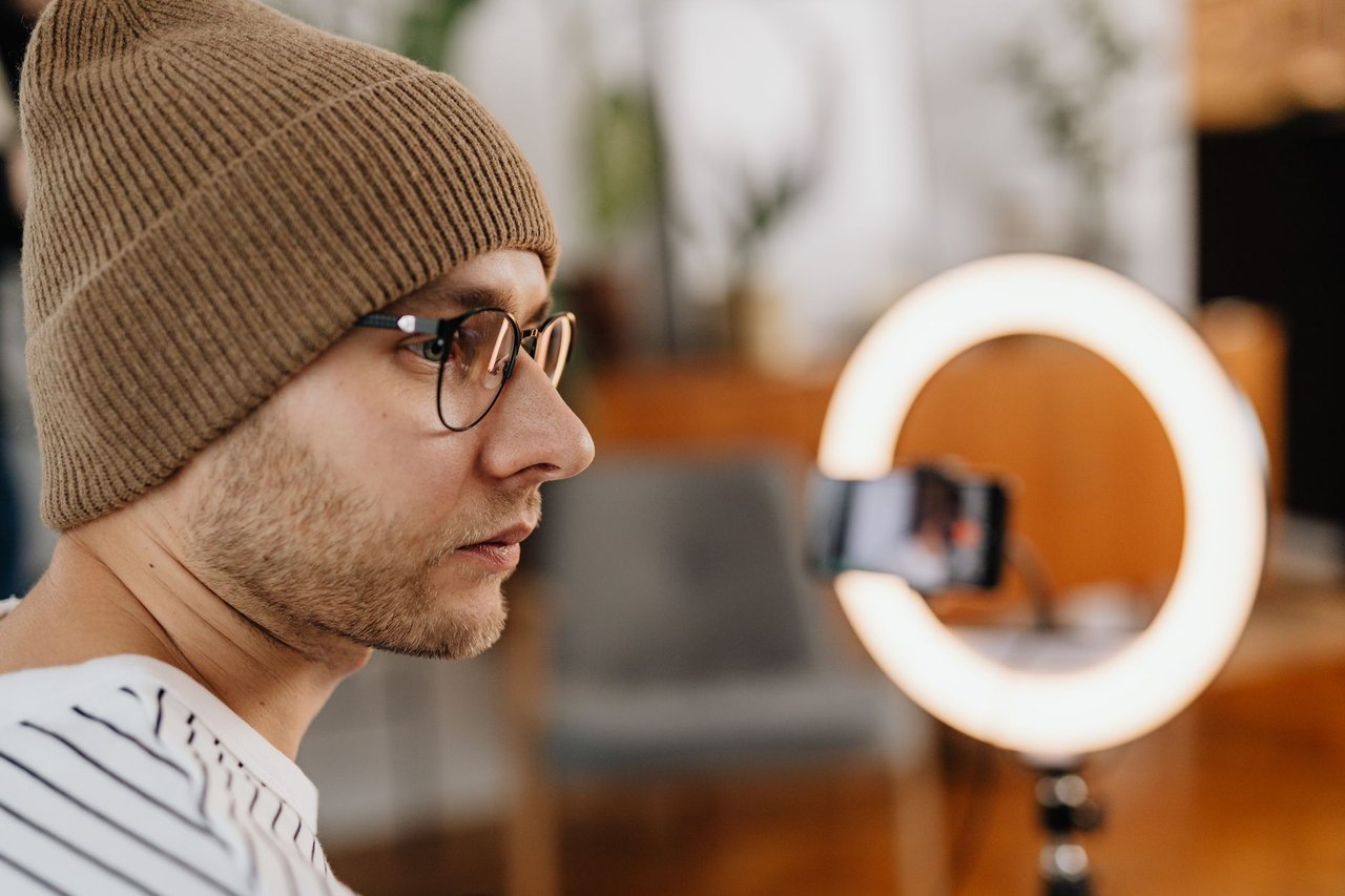 Criador grava um vídeo com smartphone diante de uma luz circular em um ambiente doméstico.