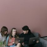 Três jovens adultos colaboram usando laptops em um ambiente interno aconchegante.