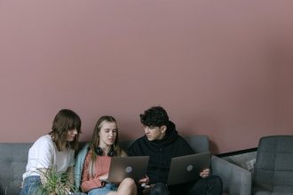 Três jovens adultos colaboram usando laptops em um ambiente interno aconchegante.
