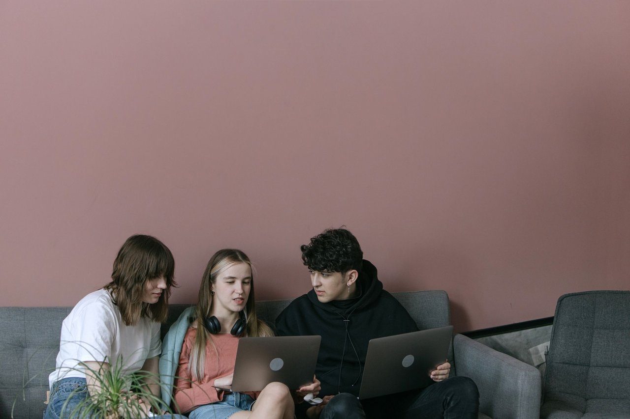 Três jovens adultos colaboram usando laptops em um ambiente interno aconchegante.