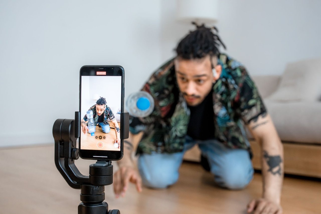 Criador de conteúdo filmando com um smartphone acoplado a um estabilizador em ambiente interno.