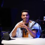 Podcaster fala diante de um microfone em um estúdio moderno.