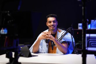 Podcaster fala diante de um microfone em um estúdio moderno.